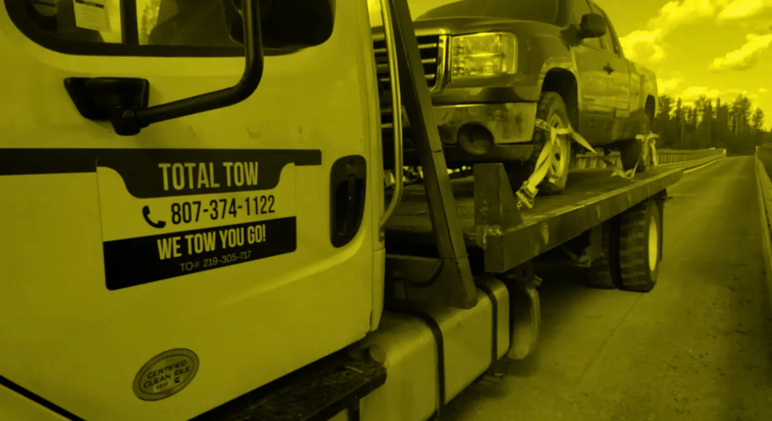 A Total Tow flatbed tow truck carrying a pickup truck, TOTAL TOW signage and phone number on the door
